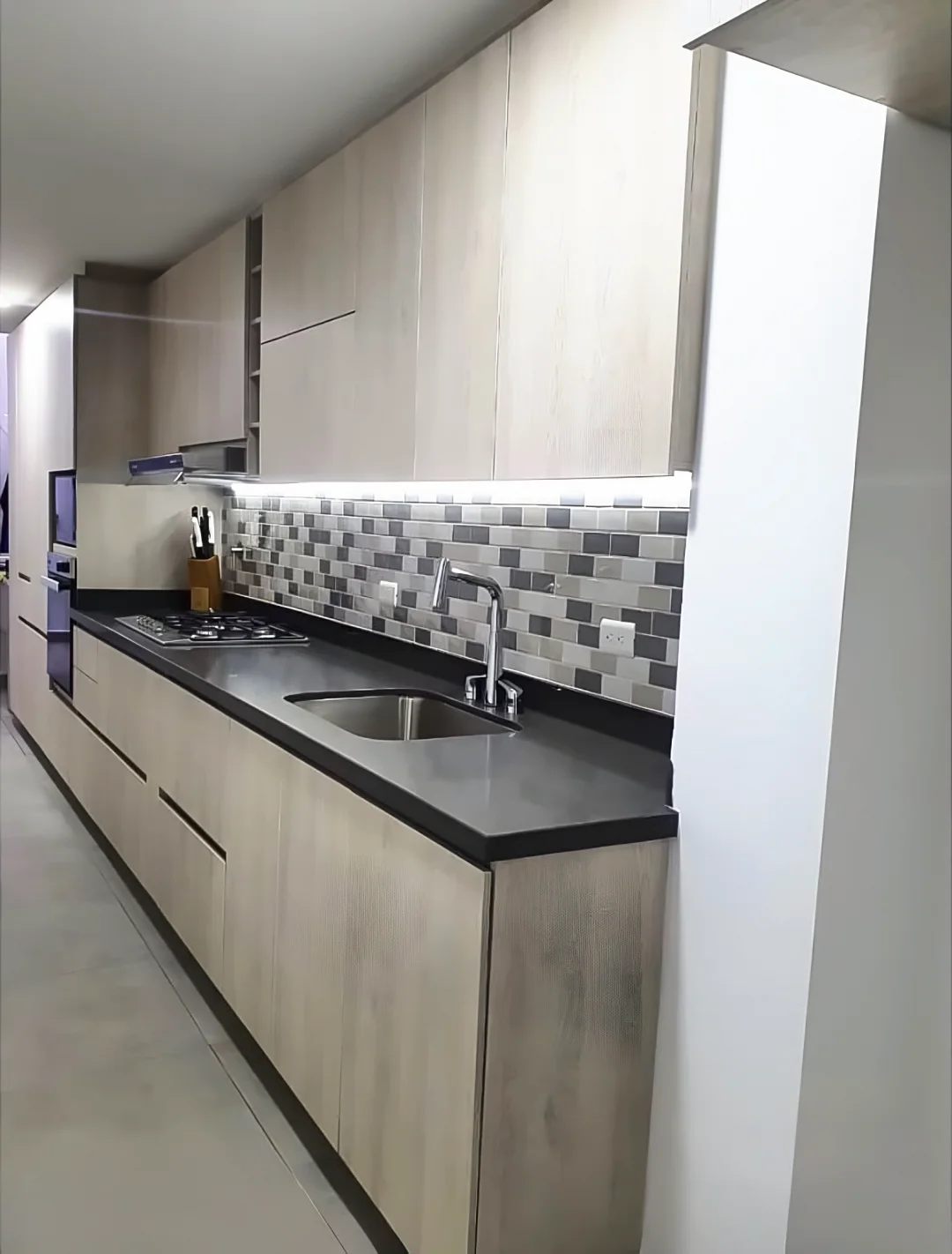 Cocina lineal vista a lo largo, con alacenas altas, luz LED bajo ellas y mesón oscuro