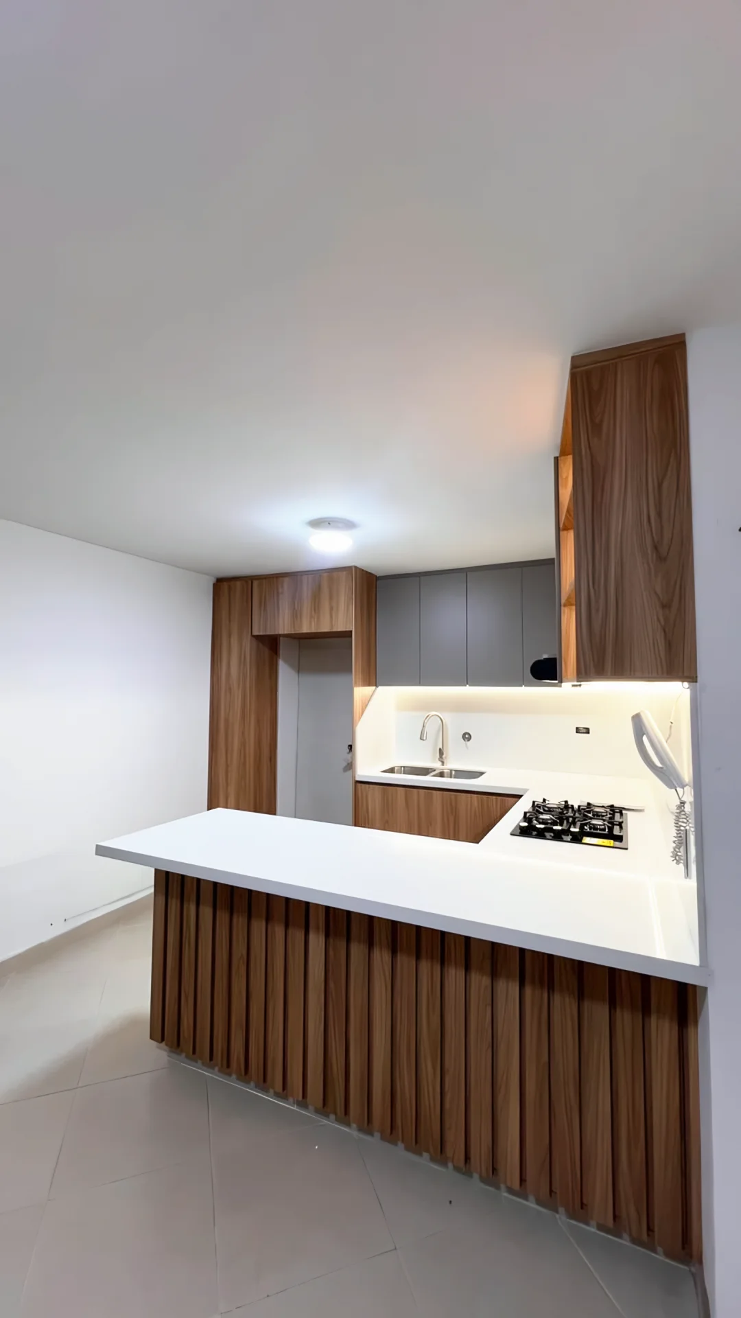 Barra de la cocina forrada en listones de madera vista desde la sala, con el mesón blanco en voladizo